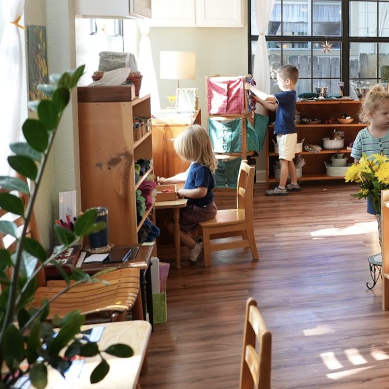 Children at work in a sunlit Montessori classroom, with an open chair at a small table