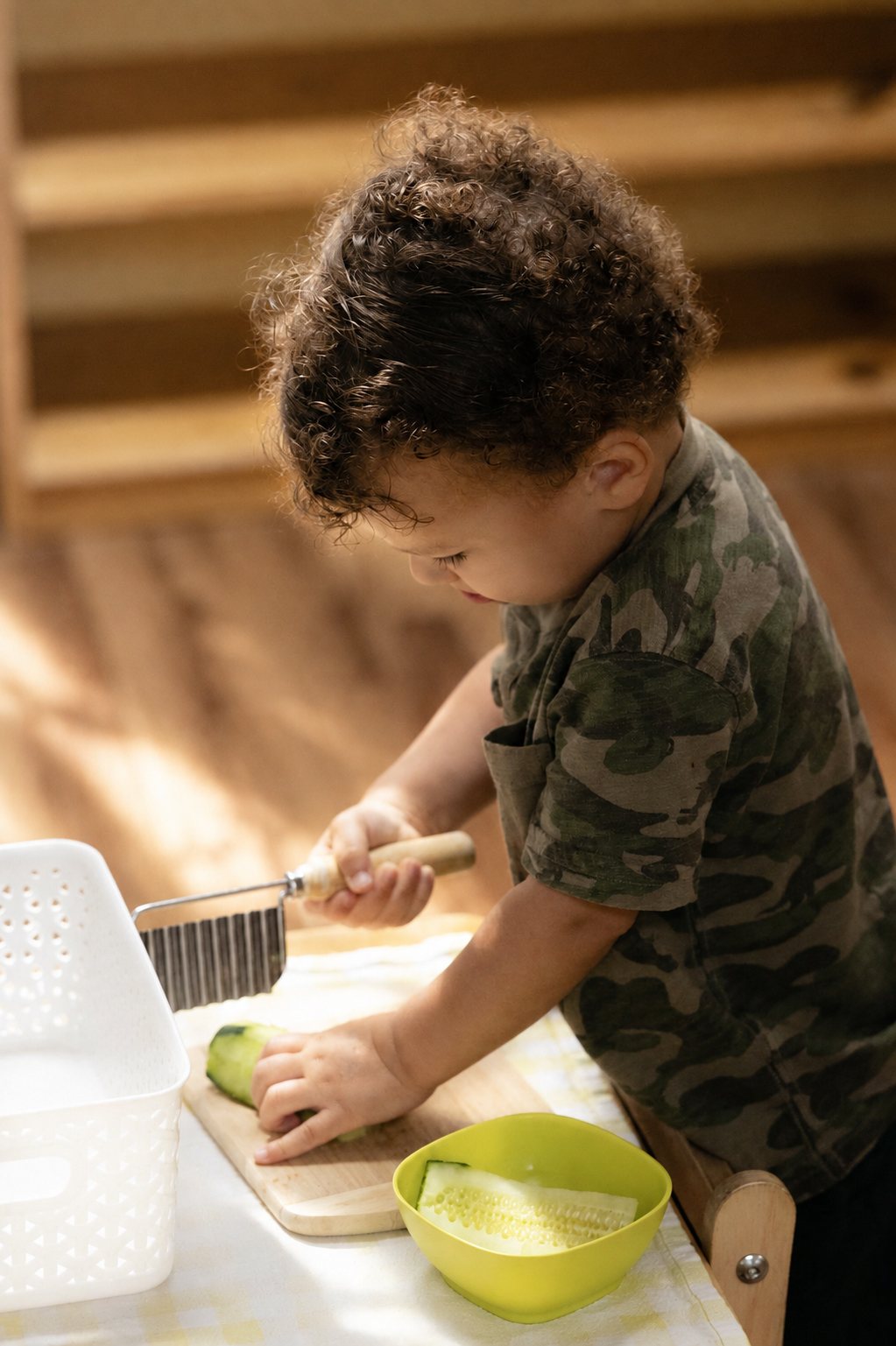 A young child slicing cucumber in the Youngest Children's Community